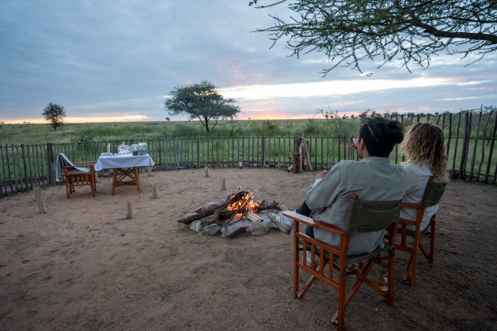 Guests at Nyumbani Camp's fire at dusk, looking out over the Serengeti